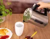 A hand pours hot water from a kettle into a mug, with croissants and jam on the table. Náhled obrázku produktu