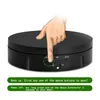 A hand is shown pressing a button on a black rotating display stand. Text below the image provides instructions for powering the device on and off. Náhled obrázku produktu