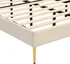 A close-up view of the corner of a beige upholstered bed frame with wooden slats and gold legs. Náhled obrázku produktu