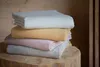 A stack of four folded blankets in different colors, resting on a wooden surface. Produktbild-Vorschau