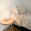 A bedside table with a lamp next to a bed with pillows and a duvet. Anteprima dell’immagine prodotto