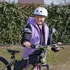 A young person wearing a helmet and a purple vest is sitting on a bicycle. Voir les images du produit