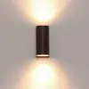 A dark brown cylindrical wall light fixture is mounted on a textured white wall, emitting light upwards and downwards. Produktbild-Vorschau