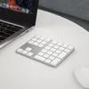 A silver wireless numeric keypad is placed on a white table next to a laptop. Náhled obrázku produktu