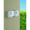 A white retractable clothesline mounted on a wall, with green bushes and a blue sky in the background. Produktbild-Vorschau