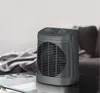 A gray electric heater sits on a glass table in a living room setting, with a blurred couch and blanket in the background. Voir les images du produit