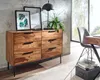 A wooden dresser with black metal legs in a room with a concrete wall and a large window. Produktbild-Vorschau