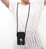 A person wearing a white t-shirt and striped pants, with a black phone case with a Karl Lagerfeld logo hanging from a black cord around their neck. Anteprima dell’immagine prodotto