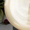 A close-up of a gold-colored dessert plate with concentric circular patterns. In the background, out of focus, are green leaves and a bunch of red grapes. Podgląd zdjęcia produktu