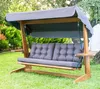 A wooden garden swing with gray cushions and a gray canopy is set up on a green lawn with trees in the background. Podgląd zdjęcia produktu