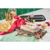 A festive scene with a stollen cake, decorated with stars and a moon, tied with a red ribbon, on a wooden board, with cinnamon sticks and star anise scattered around. A gold sequined cloth and a green napkin are also visible. Produktbild-Vorschau