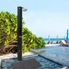An outdoor shower on a beach with lounge chairs and umbrellas in the background. Produktbild-Vorschau