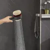 A hand holding a shower head with water spraying out, in a bathroom setting. Podgląd zdjęcia produktu