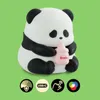 A cute panda figurine holding a baby bottle, with icons indicating features below. Produktbild-Vorschau