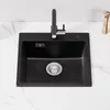A black granite kitchen sink with a black faucet is shown on a white marble countertop. Produktbild-Vorschau