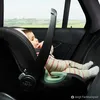 A baby in a car seat in the back of a car, with a view of the countryside through the window. Anteprima dell’immagine prodotto