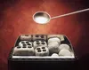 A metal ladle is held above a sauna stove filled with stones, with a red textured background. Produktbild-Vorschau
