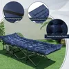 A navy blue camping cot with a thick mattress is set up on artificial grass, with close-up insets highlighting features. Náhled obrázku produktu