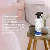 A person's arm rests on a couch next to a spray bottle and a cup on a wooden stool. Produktbild-Vorschau