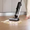 A person is using a wet and dry vacuum cleaner to clean up a spill on a wooden floor in a kitchen. Náhled obrázku produktu