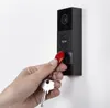 A hand holding keys and a red RFID tag is shown approaching a black video doorbell mounted on a white wall. Voir les images du produit