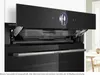 Close-up of a black built-in steam oven with its control panel open, revealing internal components and a digital display. Produktbild-Vorschau