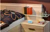 A bedside table with a digital alarm clock, books, and decorative bottles next to a bed with a patterned pillow. Anteprima dell’immagine prodotto