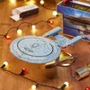A Star Trek model ship is displayed on a wooden surface, surrounded by festive lights and a Christmas cracker. Podgląd zdjęcia produktu