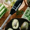 A black and silver immersion blender is shown on a wooden cutting board with various ingredients like celery, grapes, and avocados. Produktbild-Vorschau