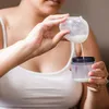 A person is pouring milk from a breast pump collection cup into a bottle. Produktbild-Vorschau