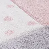 A close-up view of a textured rug with a pattern of pink polka dots on a white background, and a section of pink and gray fabric. Produktbild-Vorschau