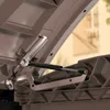 Close-up view of the hinge and gas strut mechanism of an open storage box. Náhled obrázku produktu