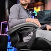 A man is sitting in a gaming chair in a room with neon lights and a computer monitor. Produktbild-Vorschau