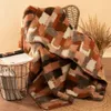A cozy scene with a wool blanket draped over a chair, next to a basket of magazines and dried grass. Produktbild-Vorschau