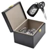 An open black box with a beige interior, containing several car keys. A separate car key fob and key are shown above and to the right of the box. Produktbild-Vorschau