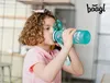 A young girl drinks from a teal water bottle with a unicorn design. Podgląd zdjęcia produktu