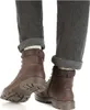 A close-up view of a person's legs wearing brown leather boots and grey cuffed pants. Produktbild-Vorschau