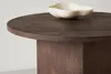 A close-up view of a round, dark wood coffee table with a white decorative bowl on top. Produktbild-Vorschau