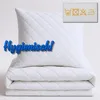 A white quilted pillow and folded blanket are stacked on a white background. A blue text overlay reads "Hygienisch!". A small label with laundry care symbols is in the upper right corner. Produktbild-Vorschau