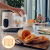 A baby food maker is shown in use on a kitchen counter, with ingredients and a baby in the background. Produktbild-Vorschau