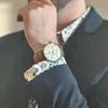 A person wearing a suit and a patterned shirt, with a watch on their wrist. Produktbild-Vorschau