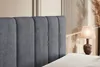 A close-up view of a dark gray velvet headboard of a bed, with a bedside lamp and decorative reeds in the background. Produktbild-Vorschau