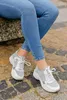 A person's legs wearing jeans and sneakers, sitting on a stone surface. Produktbild-Vorschau