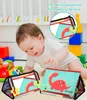 A baby is playing with a soft fabric book with mirrors and colorful illustrations of dinosaurs. Other baby toys are visible in the background. Produktbild-Vorschau