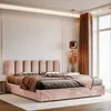 A bedroom scene with a pink upholstered bed as the main focus, decorated with pillows and a throw blanket. A bedside table with a vase of dried flowers and a pendant lamp are also visible. Anteprima dell’immagine prodotto