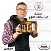 A man is holding a gift box containing three jars of mustard. Produktbild-Vorschau