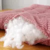 A close-up view of a pink cushion with its filling exposed, resting on a wooden surface. Produktbild-Vorschau