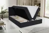 A black boxspring bed with its storage compartment open, revealing the mattress inside. The bed is in a room with a rug and a table in the foreground, and shelves and a window in the background. Voir les images du produit