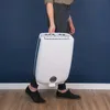 A person is carrying a white dehumidifier with blue accents. Produktbild-Vorschau