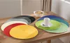 A collection of round placemats in various colors are arranged on a wooden table, with a bowl of cereal and a cup of coffee in the background. Produktbild-Vorschau